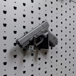 Horizontal pistol hanger mounted on GallowTech wall panel holding a handgun from a left-angle view